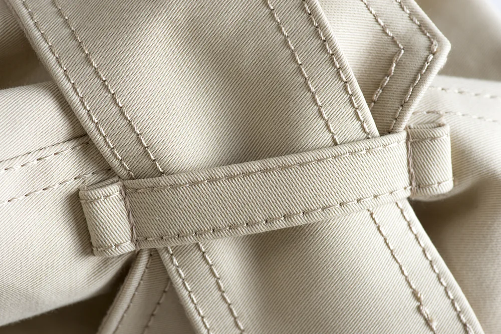 Détail : patte et surpiqûres d’un trench beige