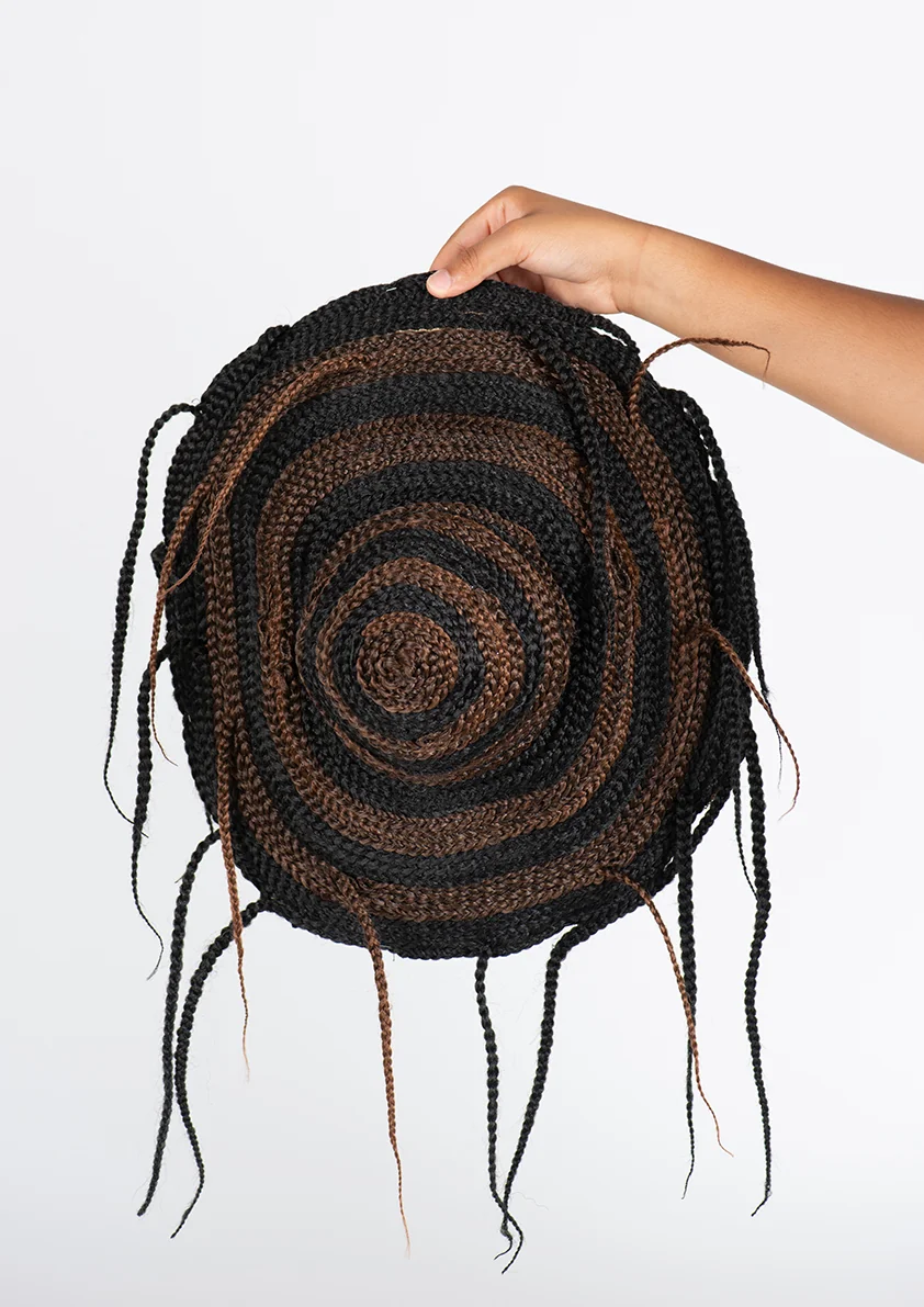 Coiffe circulaire en tresses brunes et noires tenue à bout de bras