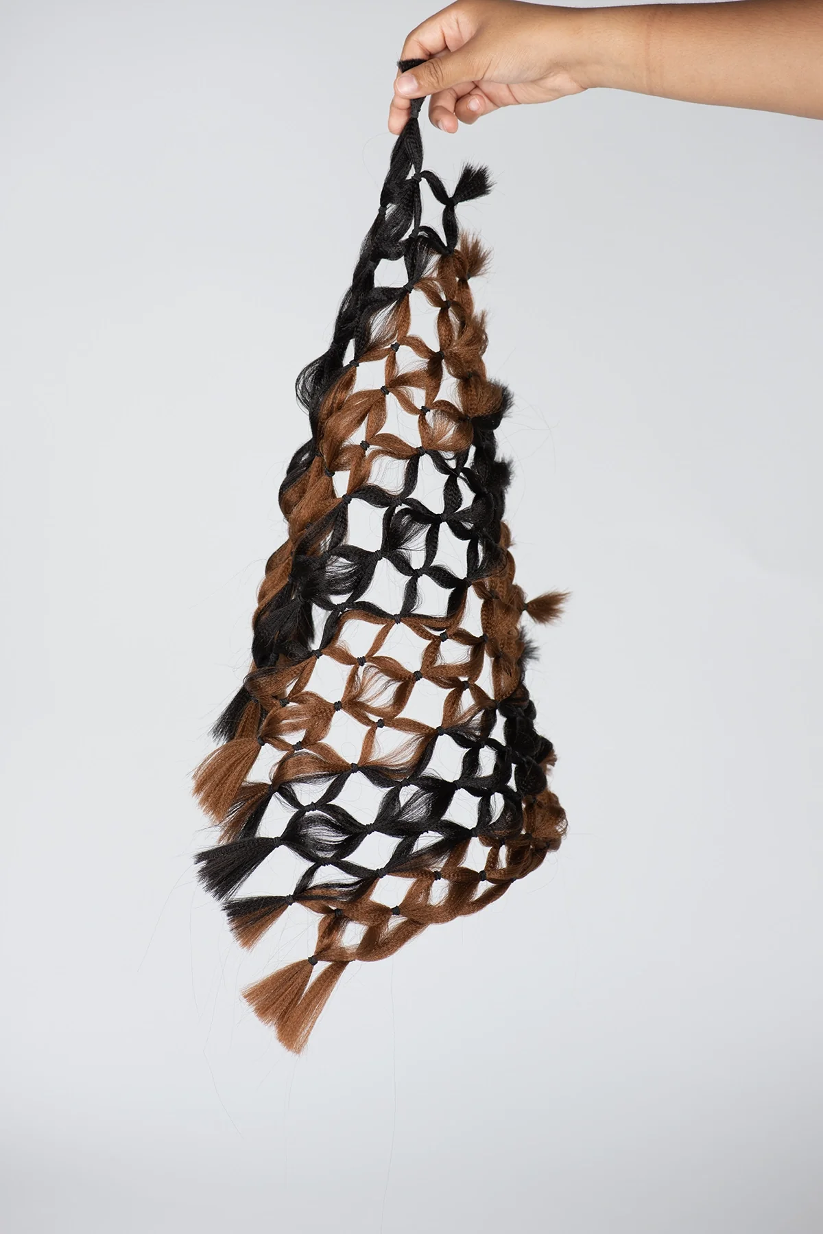 Filet de tresses noires et brunes suspendu à une main