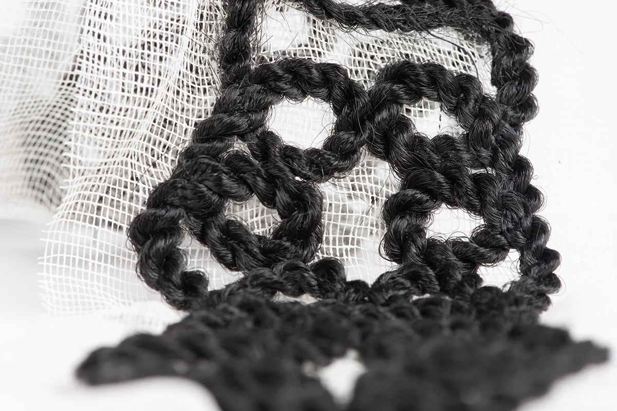 Motif ajouré de tresses noires cousues sur une gaze blanche