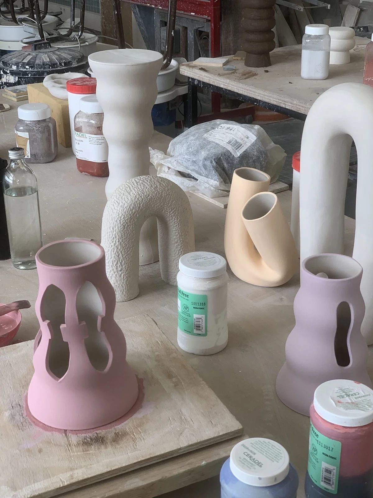 Pièces roses, blanches et beiges sur une table d’atelier, avec pots d’engobes
