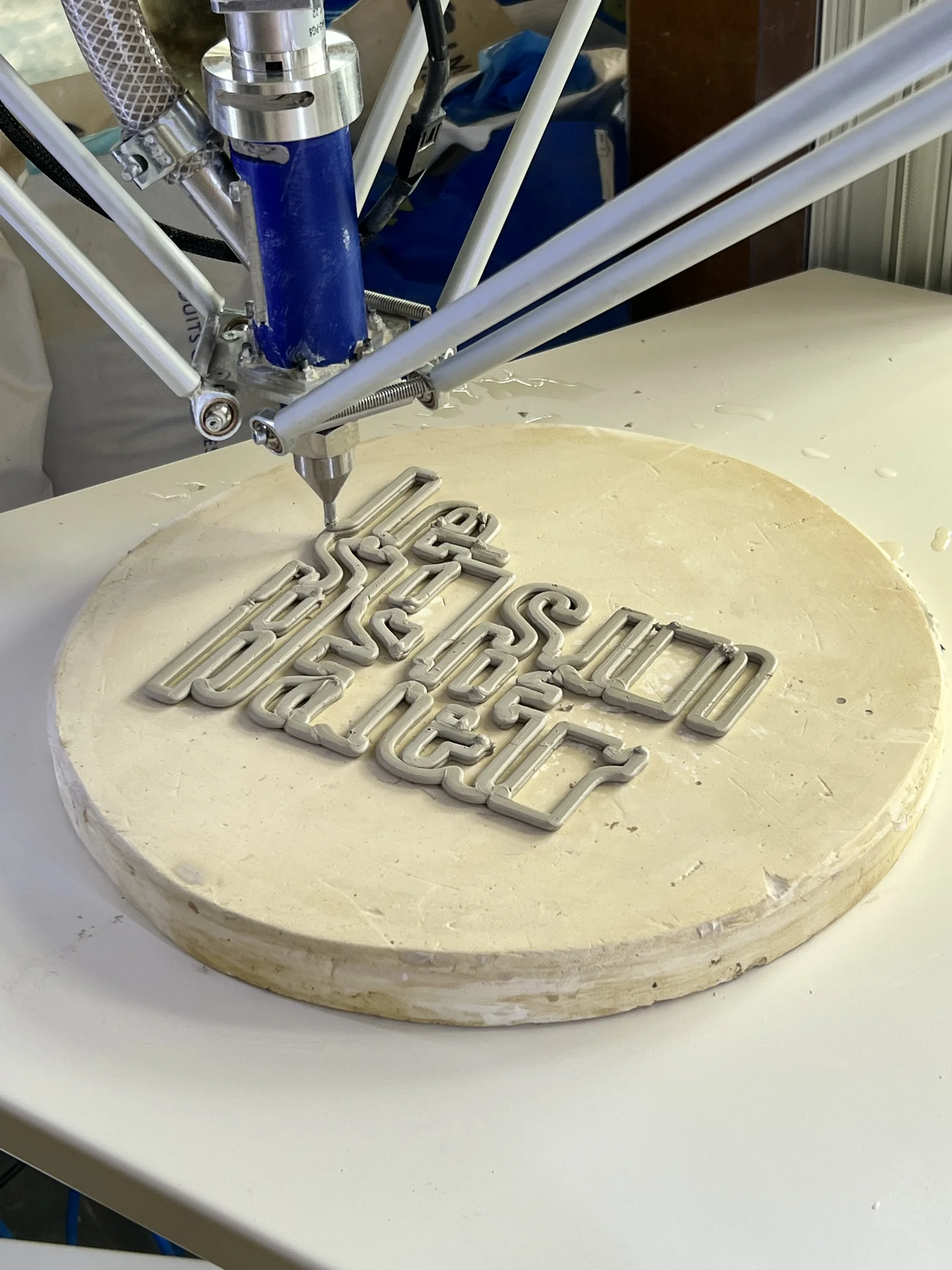 Imprimante 3D céramique déposant des lettres en grès sur un disque de terre