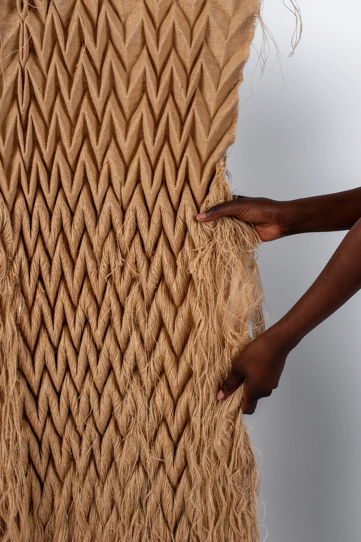 Toile de jute plissée en chevrons, tenue à la main, aux longues franges
