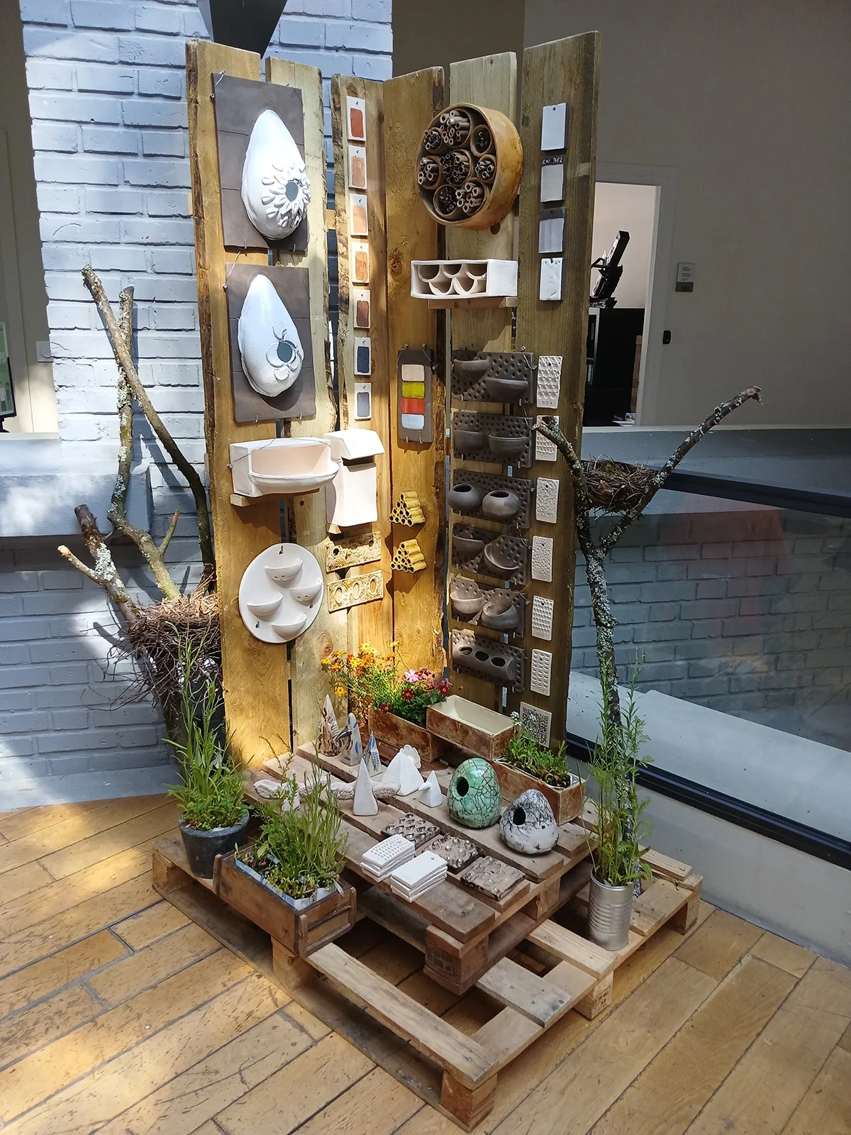 Vue d’exposition : mur de modules en céramique, nichoirs et jardinières sur palettes