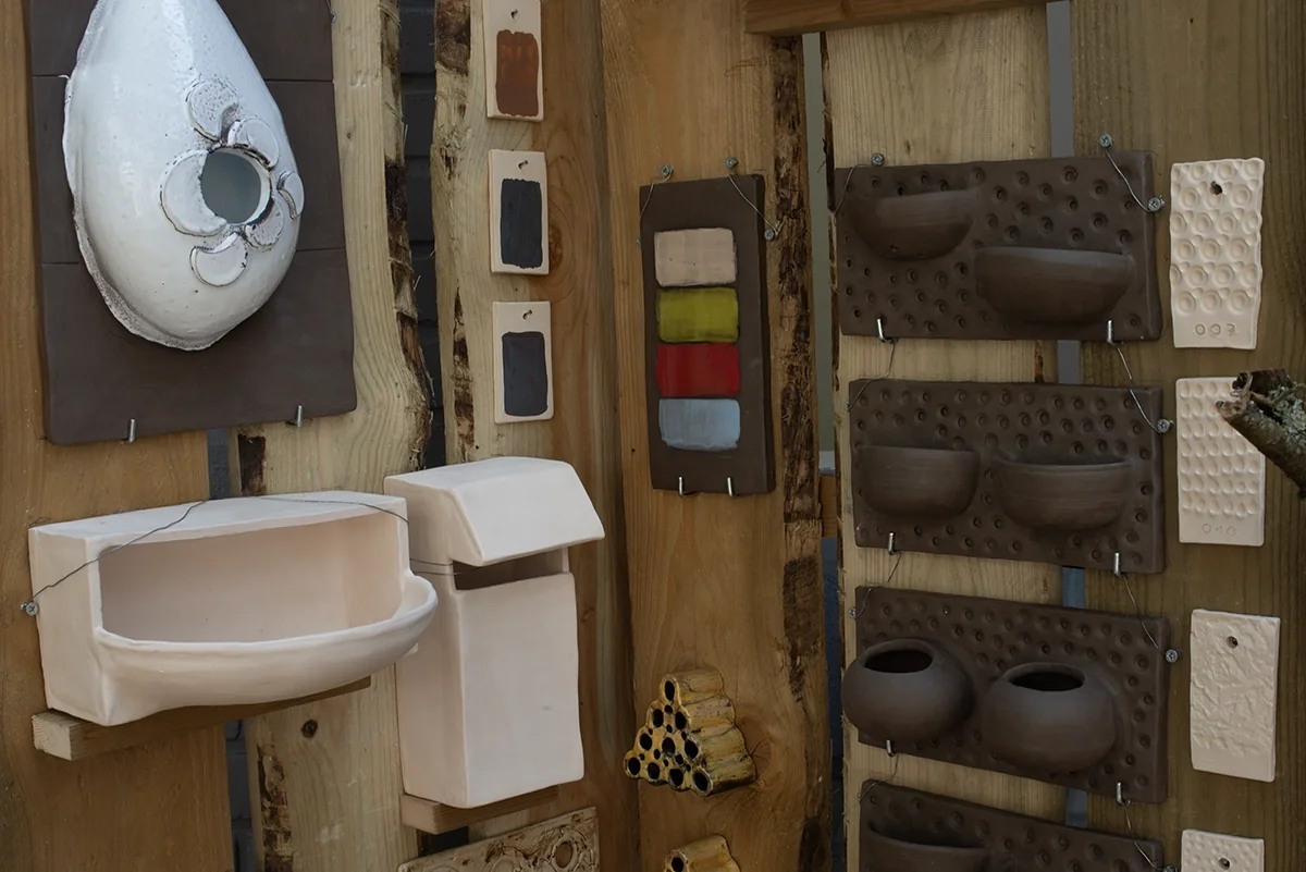 Détail du mur : nichoirs, jardinières et abri à insectes en céramique fixés sur bois