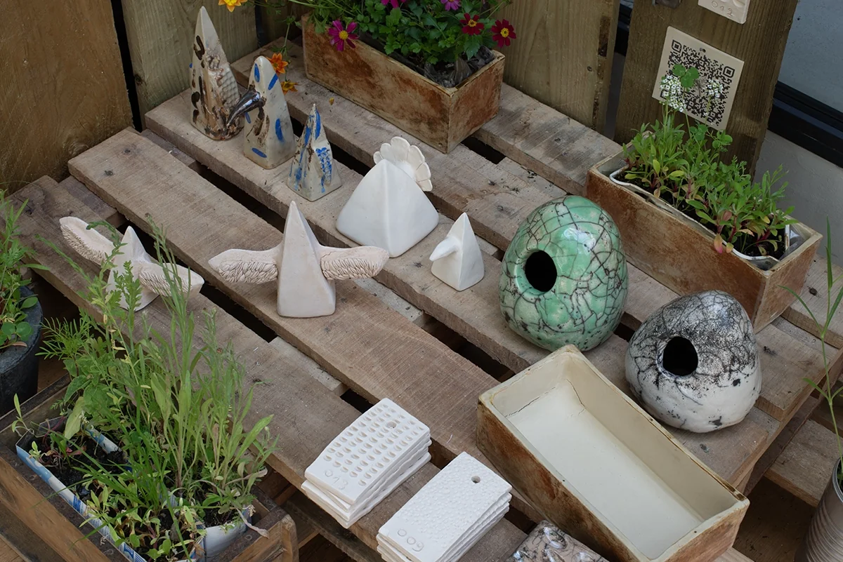Vue d’exposition : nichoirs, jardinières et pièces en céramique disposés sur des palettes végétalisées