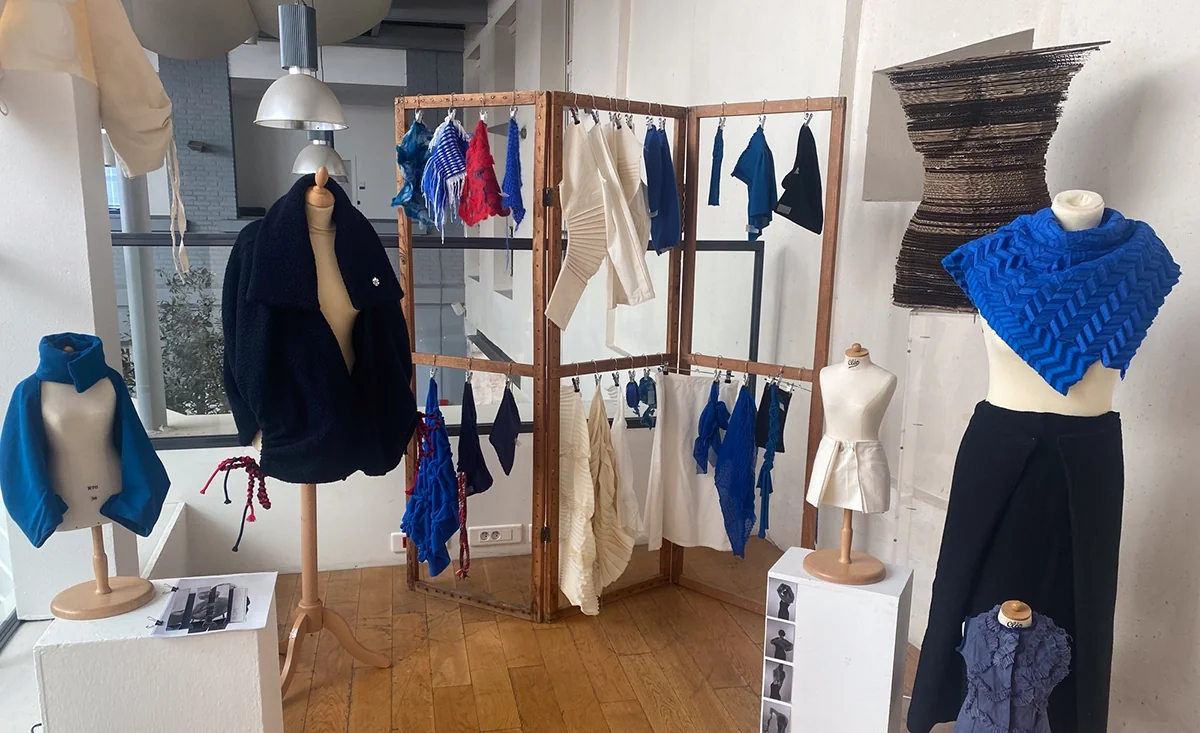 Vue d’exposition : châles, vêtements et échantillons bleus sur mannequins et portants